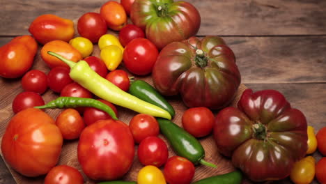 Flach-Auf-Rustikalem-Gealtertem-Palettenholz-Cherokee-Lila-Tomate-Jalapenopfeffer-Rote-Und-Gelbe-Tomaten-Cayennepfeffer-Und-Gelbe-Paprika-Mit-Hartholz-Schneidebrett