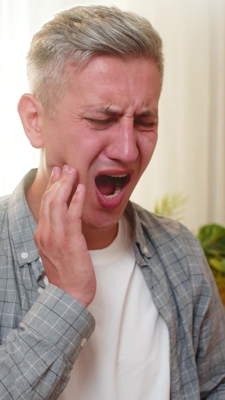 Middleaged man on home table feeling sudden tooth pain during laptop work and touching sore cheek