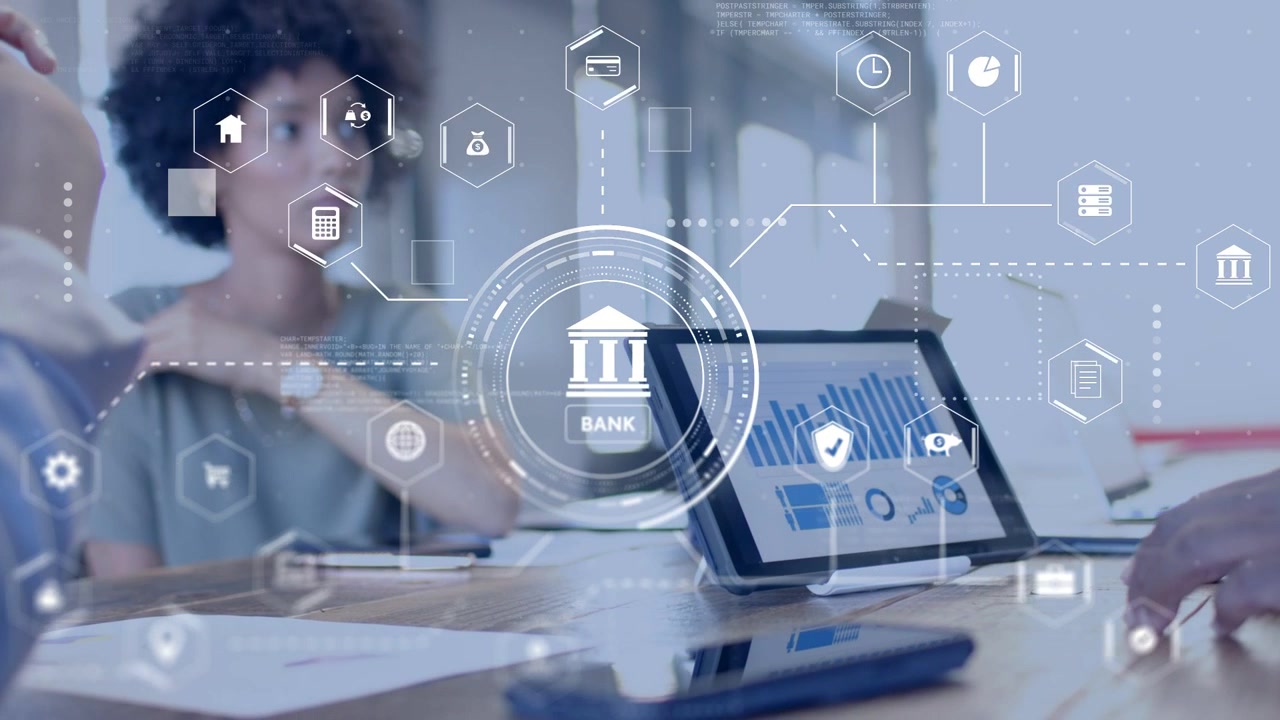 Team sitting at desk, woman reviewing data, colleague tapping tablet showing banking UI over team