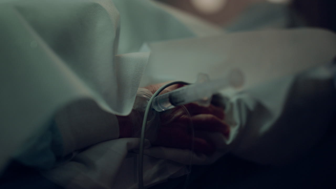 Patient hand syringe catheter closeup. Unknown man lying in hospital bed.