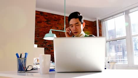 Male-executive-talking-on-mobile-phone-while-using-laptop