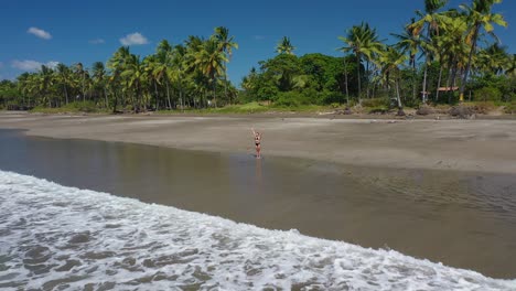 low drone shot of woman doing yoga on beach in tropics