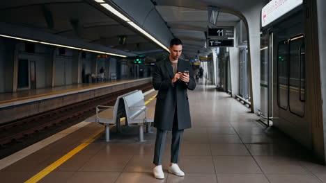 man checking his smartphone while waiting at a subway station