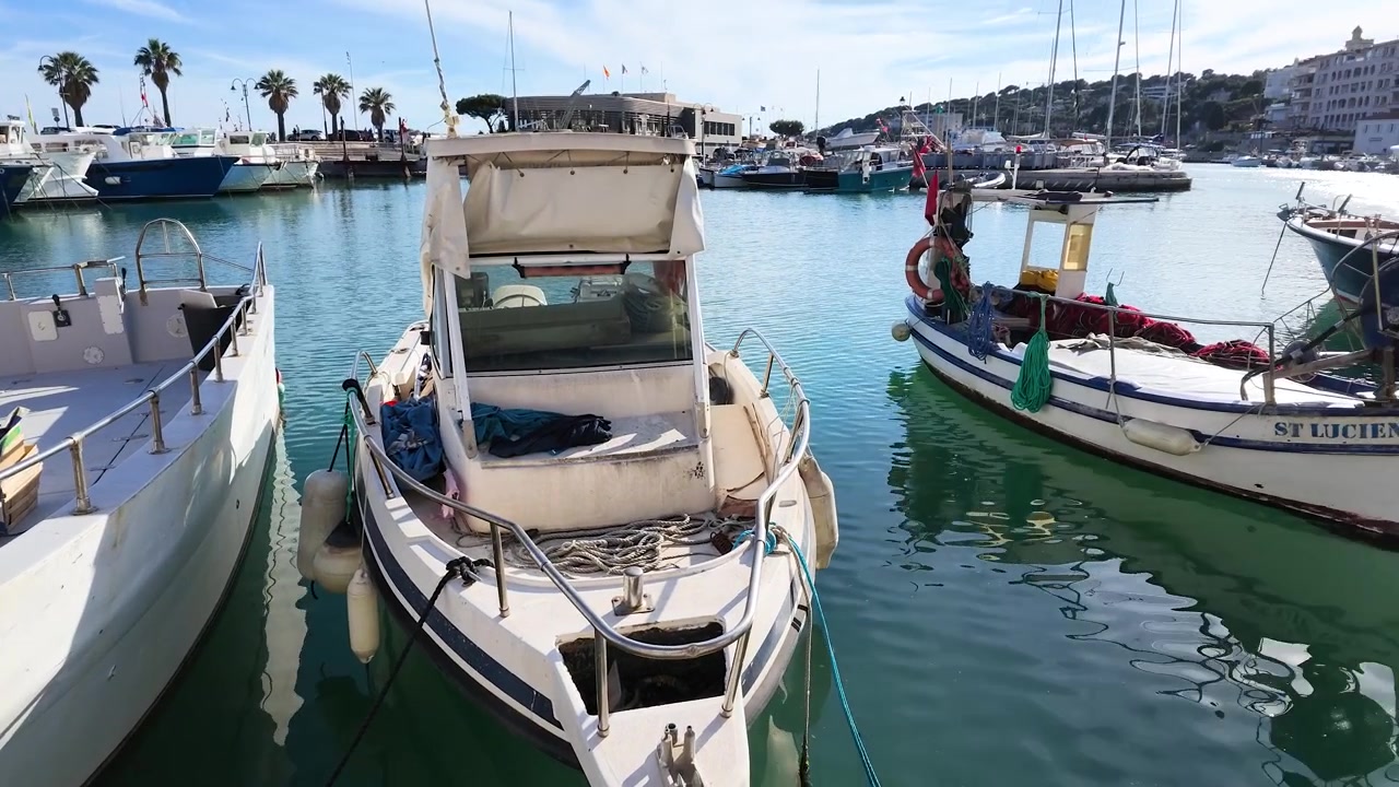 Inquadratura grandangolare di un peschereccio bianco ormeggiato in un porto mediterraneo soleggiato.
