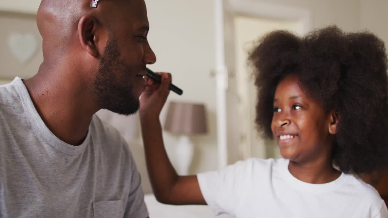 African american girl doing makeup on her father wearing crown at home