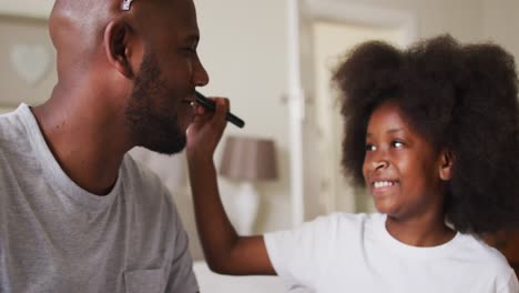 African-american-girl-doing-makeup-on-her-father-wearing-crown-at-home