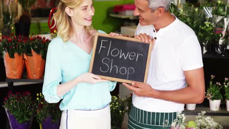 Smiling-florists-holding-flower-shop-sign-on-slate-in-flower-shop