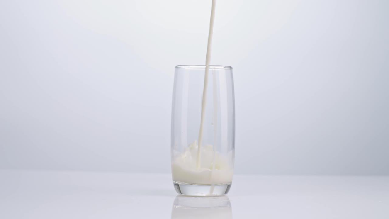 la leche se vierte en un vaso de beber sobre un fondo blanco