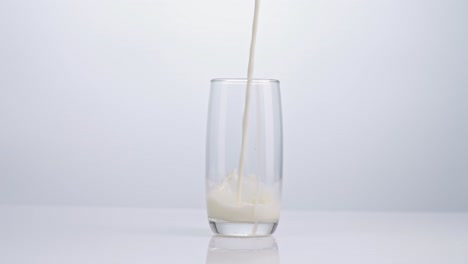 milk being poured into drinking glass on white background