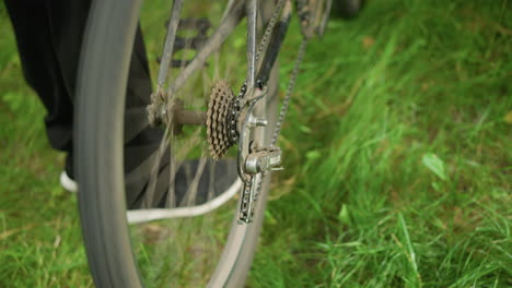 close-up of someone standing next to a parked bicycle in grassy field, gently lifting the rear tire and pedaling briefly, causing the tire to rotate, then drops it on a grassy field