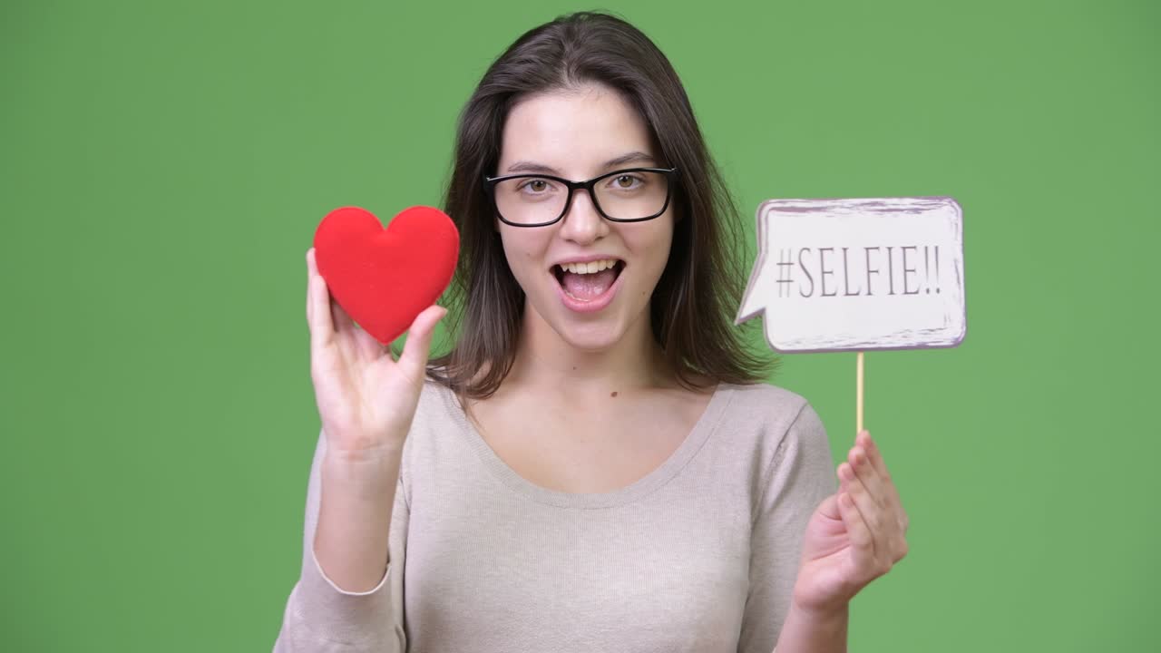 Young happy beautiful woman holding red heart and selfie paper sign