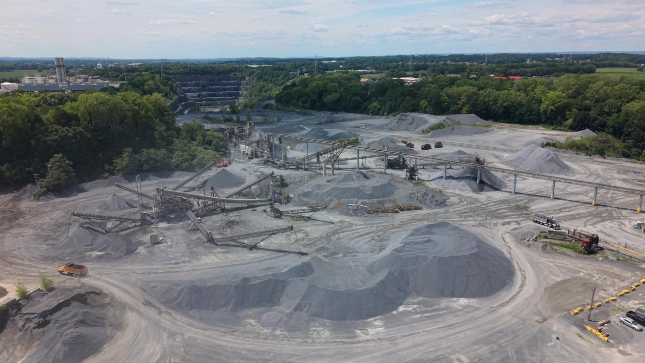 Cinematic drone footage sweeping over an open pit stone quarry, gravel piles, and heavy mining machinery.