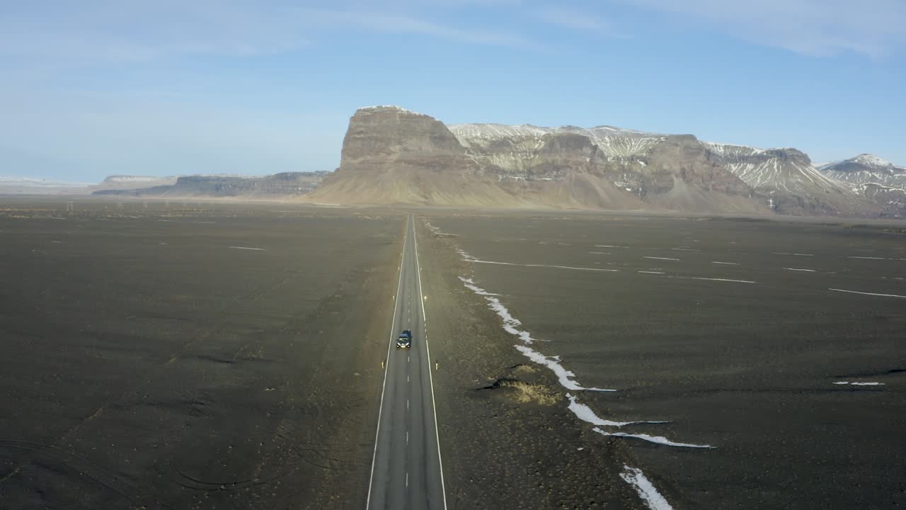 Straight and narrow road through flood plain desert towards mountain range in Iceland.