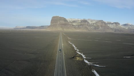 straight and narrow road through flood plain desert towards mountain range in iceland.