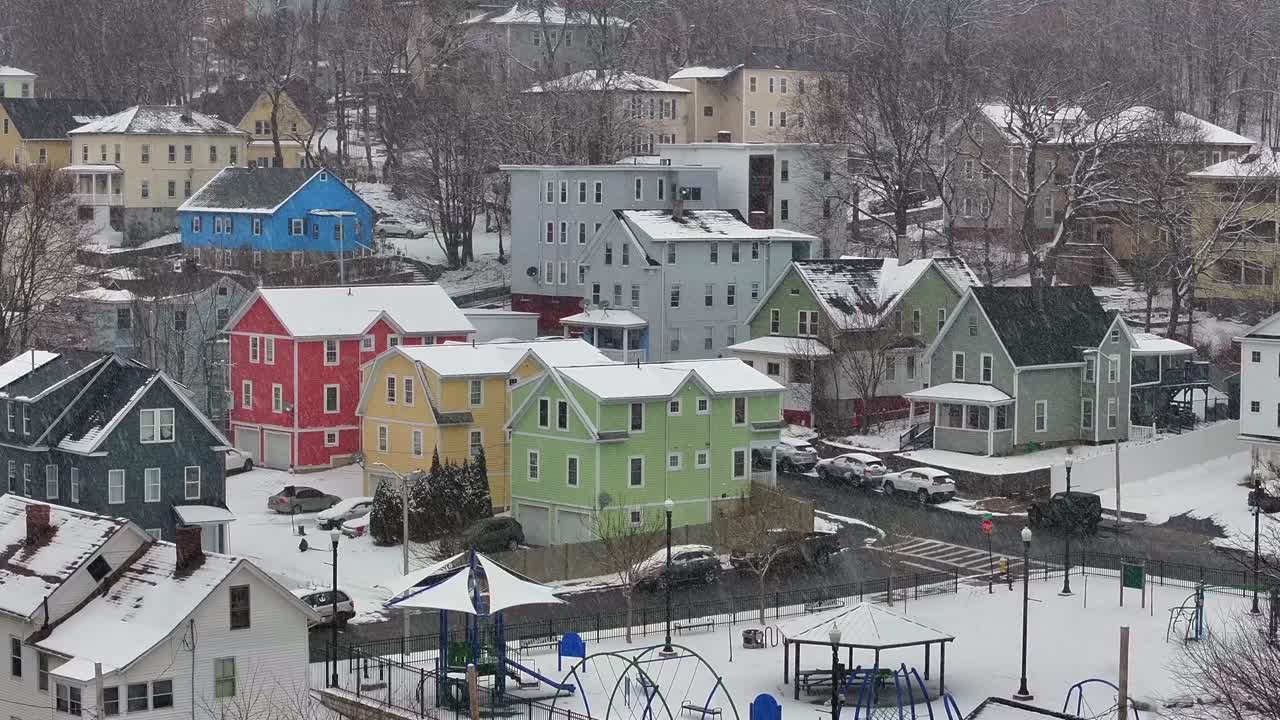 Colorful triple-decker homes line a snowy hillside in Worcester, Massachusetts. Aerial during snow storm.