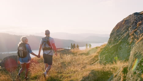 slow motion rear view shot of young couple walking on top of hill on hike through beautiful countryside in lake district uk