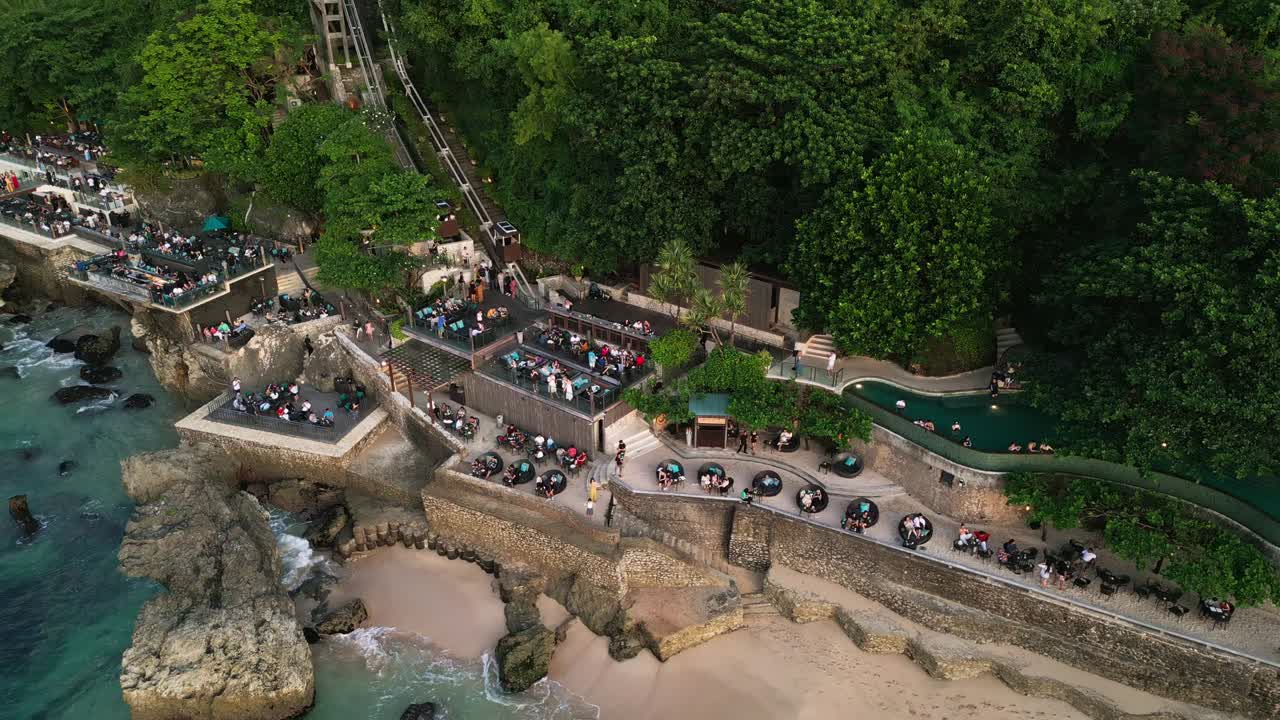 At sunset time people gather at a bali rock bar to enjoy dinner above the ocean where the natural rock setting and sound of waves create a calm and memorable evening experience.