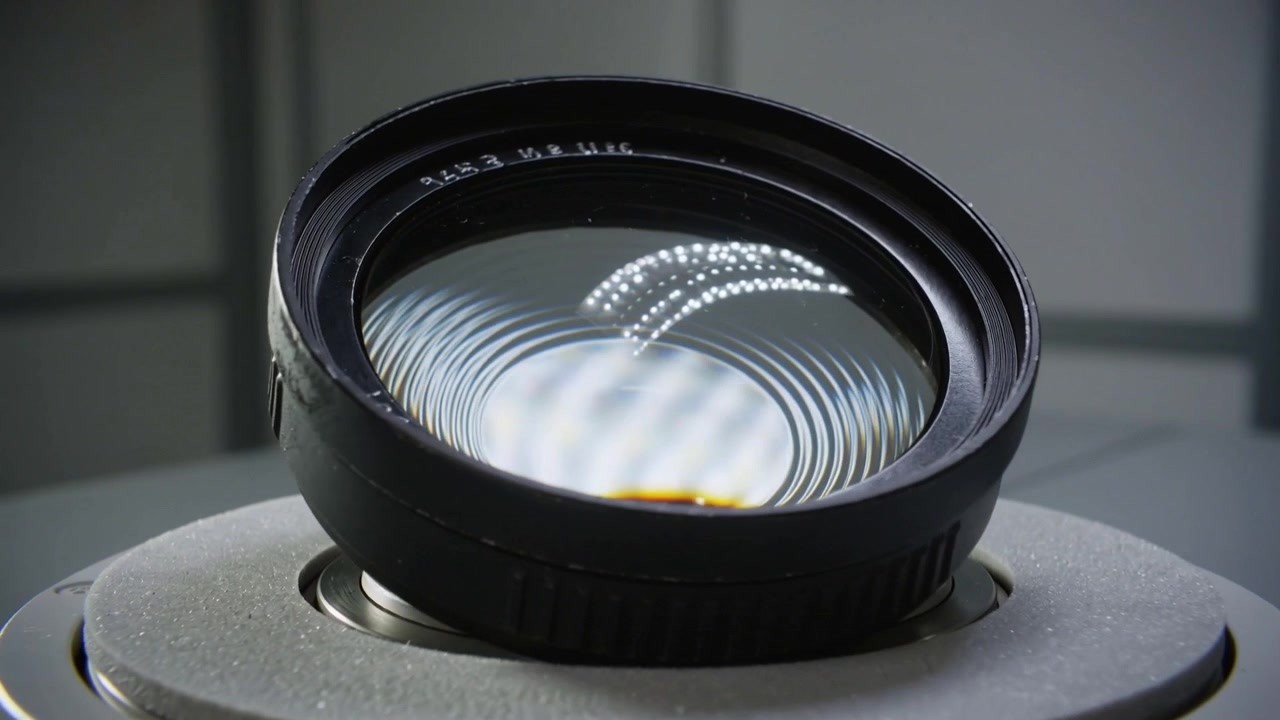 Rotating optical lens after twist showing ring patterns and dotted LED arc on mount at workshop