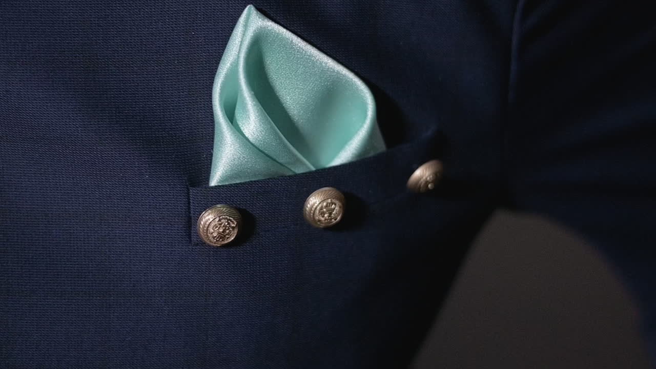 A blue suit with gold buttons and a teal pocket square on an Indian groom at a reception. Slow Motion.