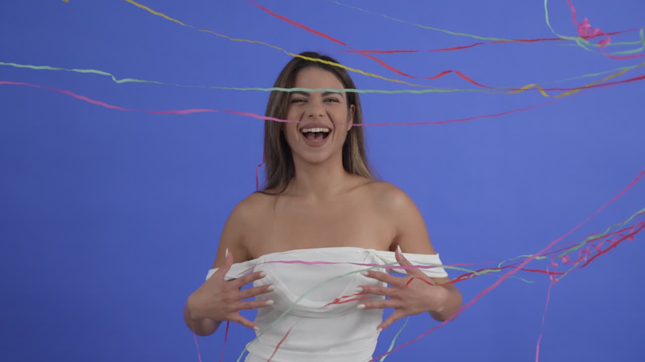 Celebration as a pretty young woman is showed in party streamers. Slow motion, isolated on blue background.