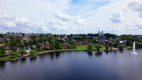 wide aerial view of zarasai town with lake and water fountain, historic church on the hill, and residential buildings nestled in forest. shot in zarasai, lithuania (zarasai, lietuva)