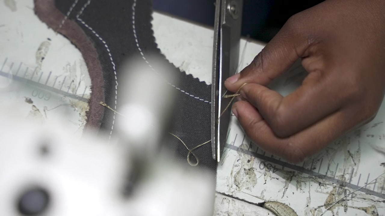 Un primo piano di mani che infilano materiale in pelle su un banco da lavoro, preparandolo per la cucitura. Ideale per contenuti sull'artigianato e le tecniche tradizionali nella lavorazione della pelle
