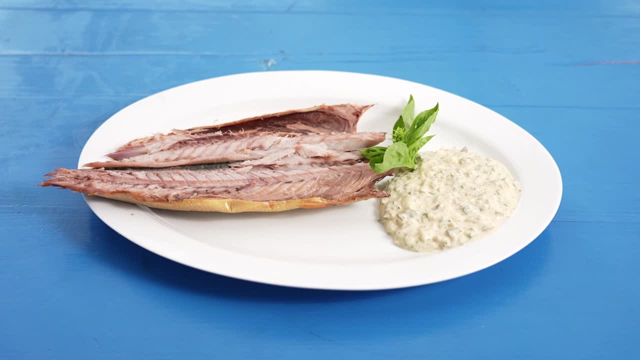 Delizioso filetto di pesce affumicato servito con salsa tartara cremosa ed erbe fresche su un piatto bianco sopra un tavolo di legno blu. Perfetto per temi di cucina di mare, gourmet o ristoranti