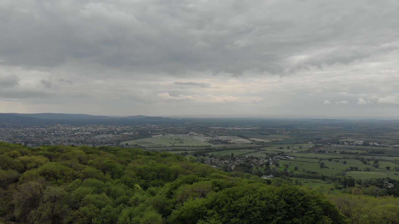 Slow drone shot in The Cotswolds. Moving forward, over trees, green grass, white clouds and sunset.