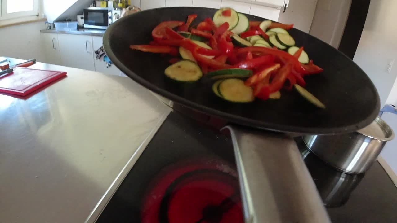 Slow-motion video of a chef stirring vegetables in a frying pan in a non-commercial kitchen. Flowing the pan or from the hands perspective.
