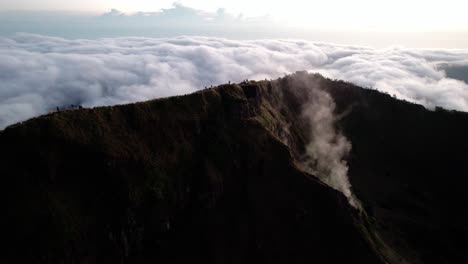 hikers on viewpoint of mount batur volcano with sea of clouds in the background at sunrise in indonesia