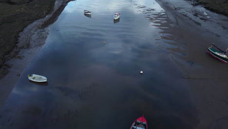 Langer-Drohnenschuss-Aus-Der-Luft,-Der-Bei-Ebbe-Mit-Segelbooten-In-North-Norfolk-An-Einem-Bewölkten,-Düsteren,-Launischen-Tag-über-Den-Bach-Fliegt