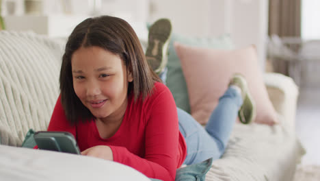 Video-of-happy-asian-girl-resting-on-sofa-with-smartphone