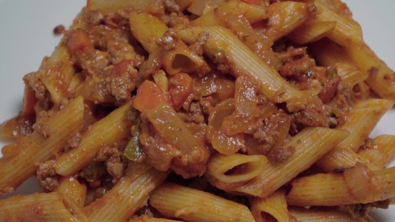 nedad, pasta bolognese med penne nudler på hvid tallerken, nærbillede