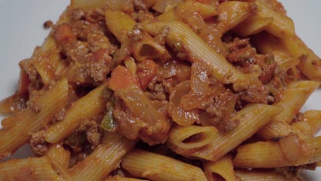 Nach-Unten-Kippen,-Pasta-Bolognese-Mit-Penne-Nudeln-Auf-Weißem-Teller,-Nahaufnahme