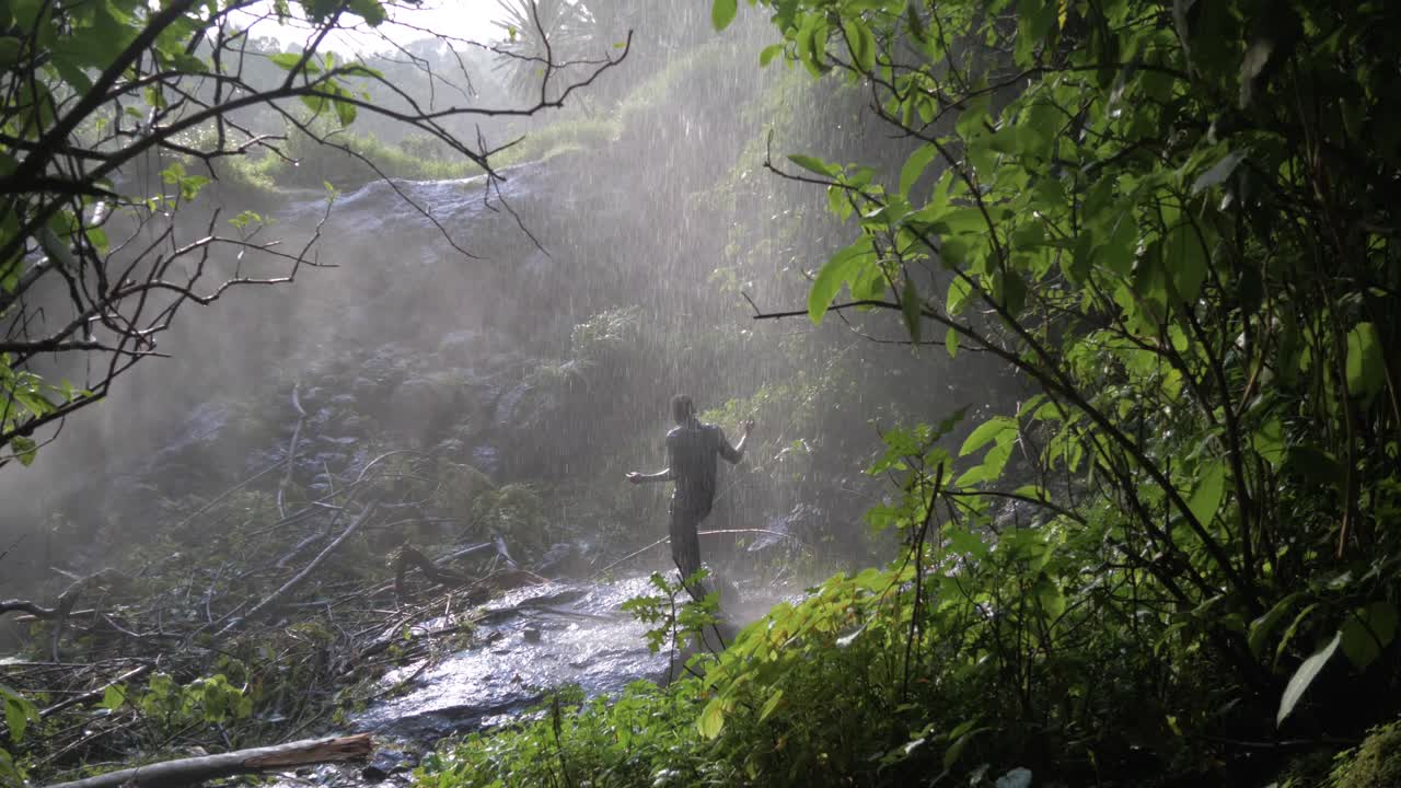 아프리카 남자는 젖으면서 열대 폭포 아래에서 행복하게 춤을 춥니다.