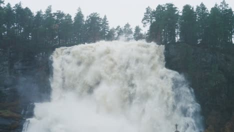 una diminuta silueta de una persona bajo la enorme cascada de tvinderfossen