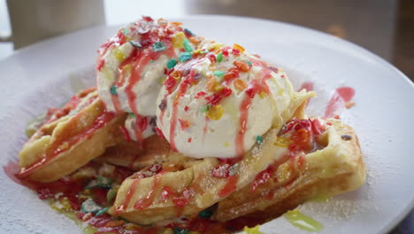 gofres belgas de confeti rellenos y cubiertos con cereales de guijarros afrutados y helado rociados con fresa y jarabe de arce, cierre deslizante 4k