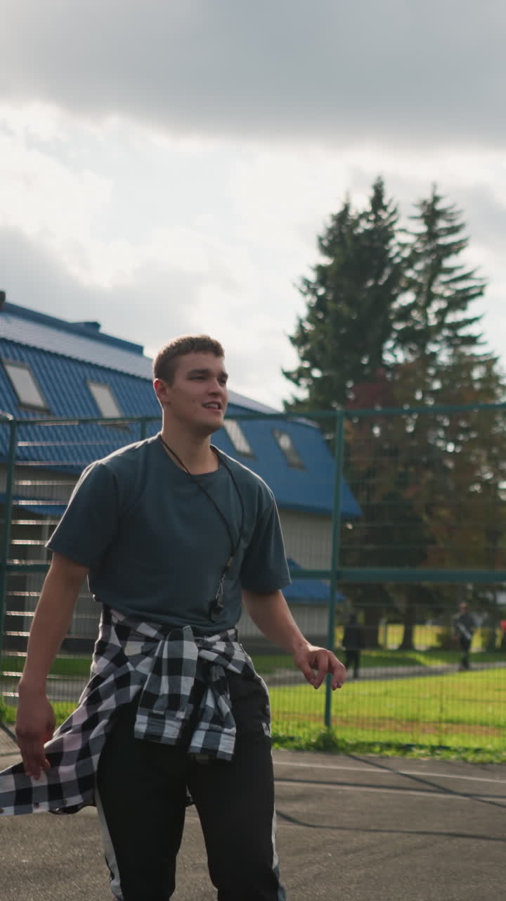 joven con camisa alrededor de la cintura salta para golpear el voleibol en la arena deportiva con el fondo de personas caminando, cancha al aire libre y equipos deportivos visibles