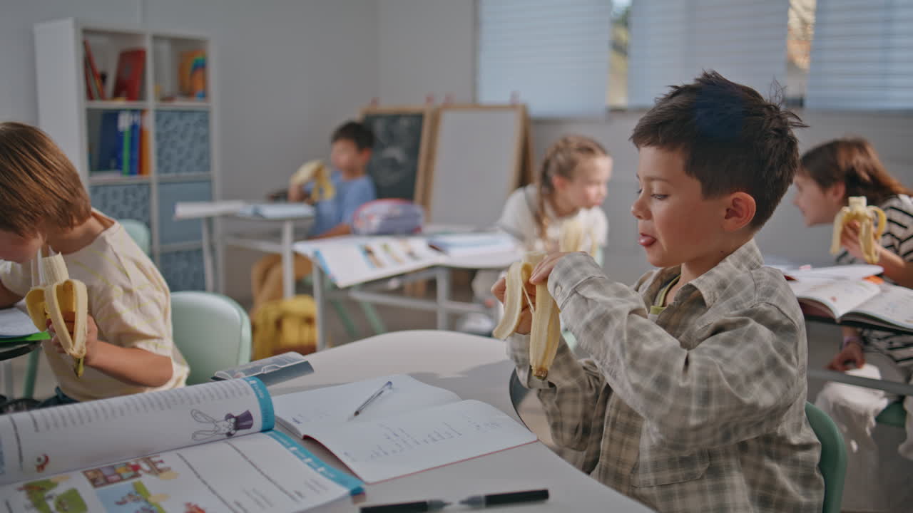 Hungry children lunch break at school closeup. Two boys eating bananas at desks