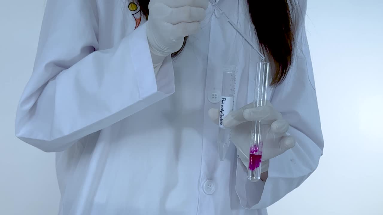 A scientist in a lab coat performs a chemical reaction causing a vibrant pink transformation