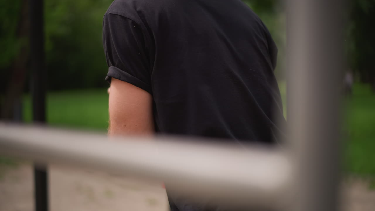 Person Taking Break At Outdoor Fitness Station, Male Exerciser Pauses Workout Amidst Park Setting Scenery, Man Takes Momentary Pause While Using Outdoor Fitness Equipment In Park Environment