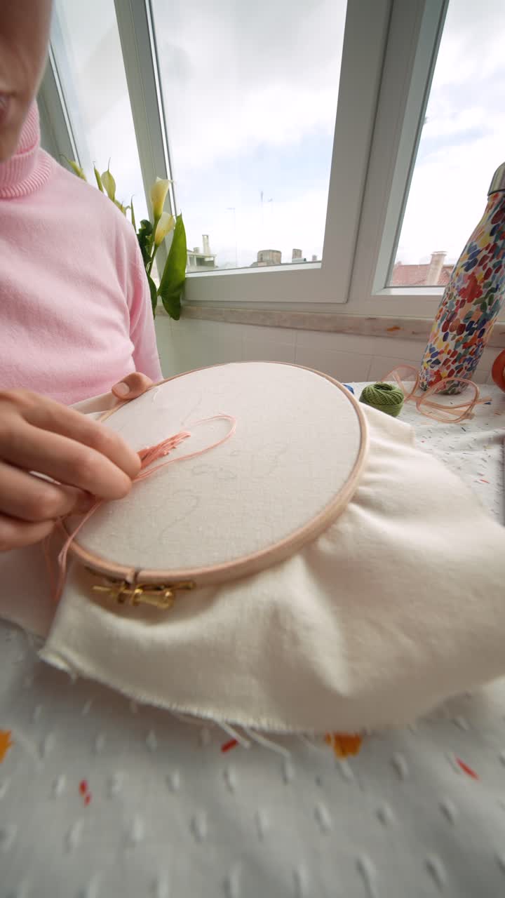 Primo piano di donna che ricama tessuto con filo rosa