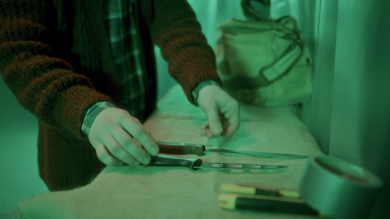 Serial Killer Arranging Sharp Weapons on Table in Dimly Lit Room