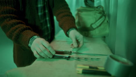 serial killer arranging sharp weapons on table in dimly lit room