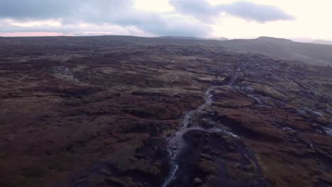 Río-De-Sobrevuelo-Aéreo-Que-Fluye-A-Lo-Largo-De-La-Meseta-De-Páramos-De-Kinder-Scout-En-Inglaterra-Durante-El-Día-Nublado