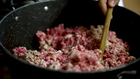 close up of minced meat mixing in a pot with a wooden spoon, preparing ingredients for a delicious meal