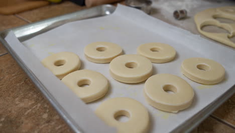 hands placing raw donut shaped pieces of dough on baking tray, slowmo closeup