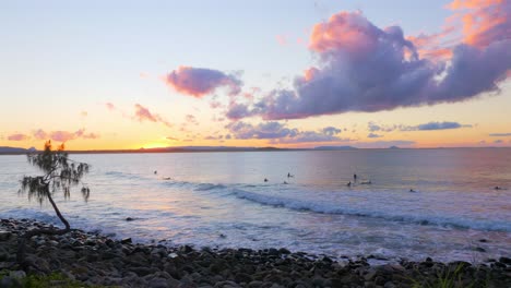 tourists surfing on the wavy beach with rocky seashore at dusk in queensland