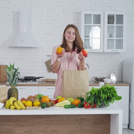Woman with orange and apple in her hands indoors. Beautiful housewife chooses an apple to eat. Healthy food concept.