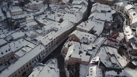 Volando-Sobre-La-Iglesia-Cristiana-Y-Los-Tejados-Cubiertos-De-Nieve-En-La-Ciudad-Minera-Banska-Stiavnica,-Tiro-Aéreo